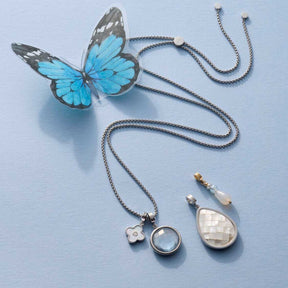Schmuckset Anhänger JANE mit blauem Schmetterling und silbernen Kettenanhängern auf hellblauem Untergrund