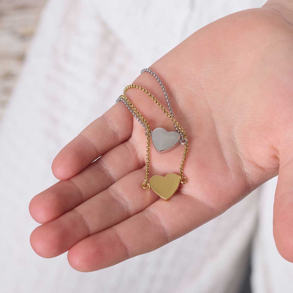 Hand hält zwei silberne Armbänder mit Herzanhängern