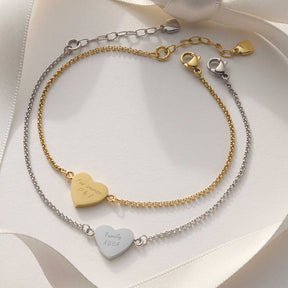 Zwei Armbänder KELLY mit gravierten Herzanhängern in Gold und Silber auf weißem Stoff