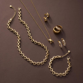 Goldene Schmuckkollektion mit Ohrsteckern SOPHIE, Ketten und Ringen auf grauem Hintergrund