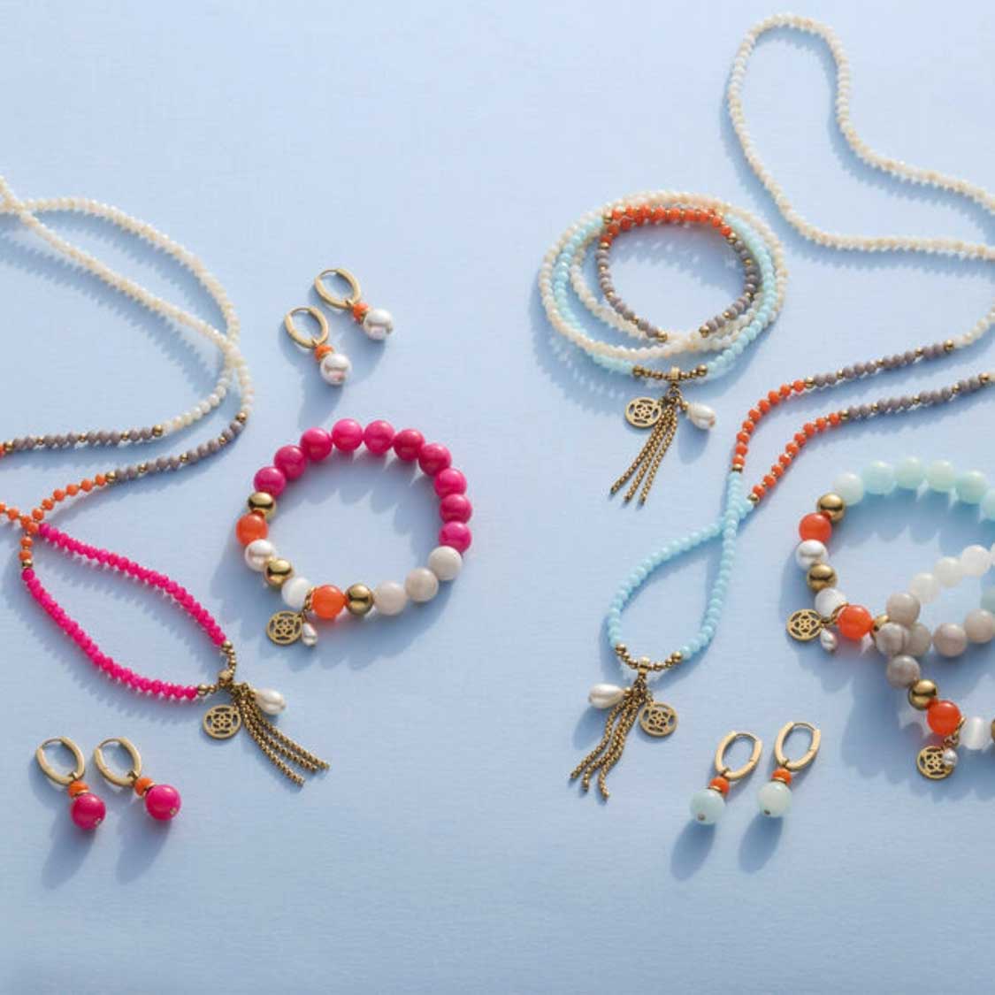 Schmuckkollektion mit Creolen, Armbändern und Ohrringen in Blau-, Pink- und Orangetönen auf hellem Untergrund