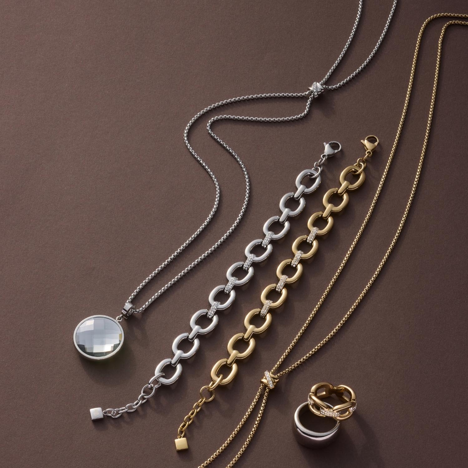 Halskette DARIA 90 cm gold mit Zirkonia-Anhänger und Kettengliedern, Schmuckstücke auf braun strukturiertem Untergrund