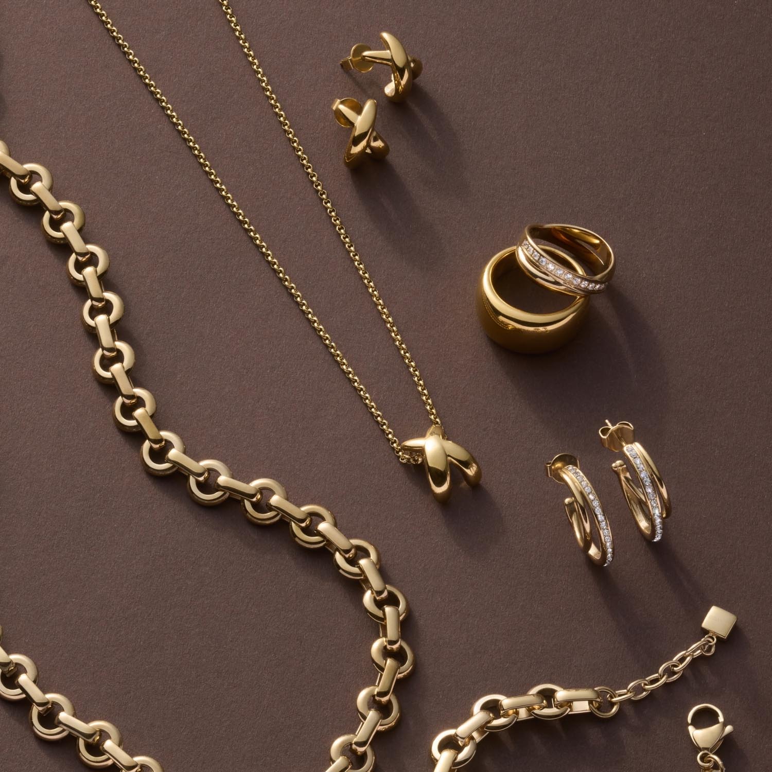 Goldener Schmuck auf grauem Untergrund: Ketten, Ring DARIA 18, Ohrringe und Anhänger