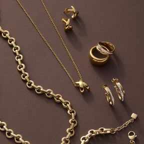 Goldschmuck Kollektion mit Ring DARIA 20, Ketten und Ohrringen auf grauem Hintergrund