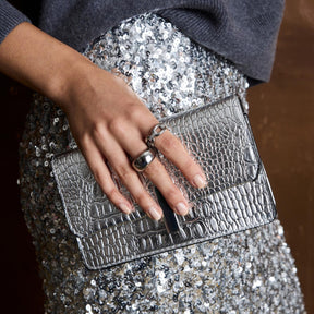 Frau traegt Ring BELLE 17 an der Hand, haelt silberne Clutch mit Krokodilmuster