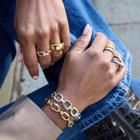 Person traegt goldene Ringe und Armband an den Haenden, blaue Jeans