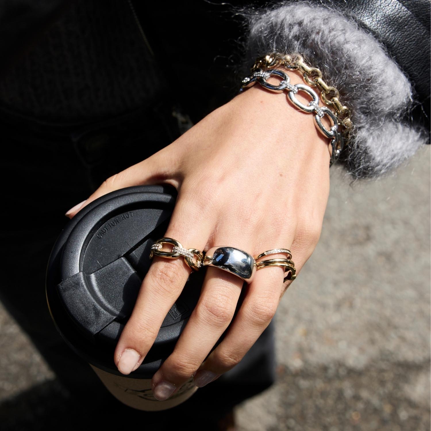 Hand mit mehreren goldfarbenen Ringen und schwarzer Handtasche, Nahaufnahme