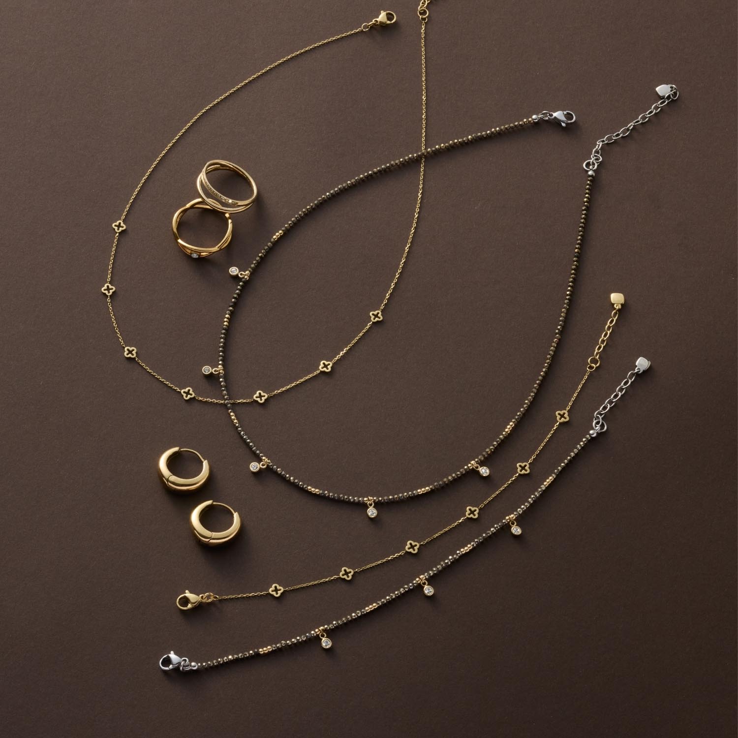 Armband ANNA CIAO in Gold- und Silbertönen mit Ringen und Schmuckstücken auf braunem Untergrund
