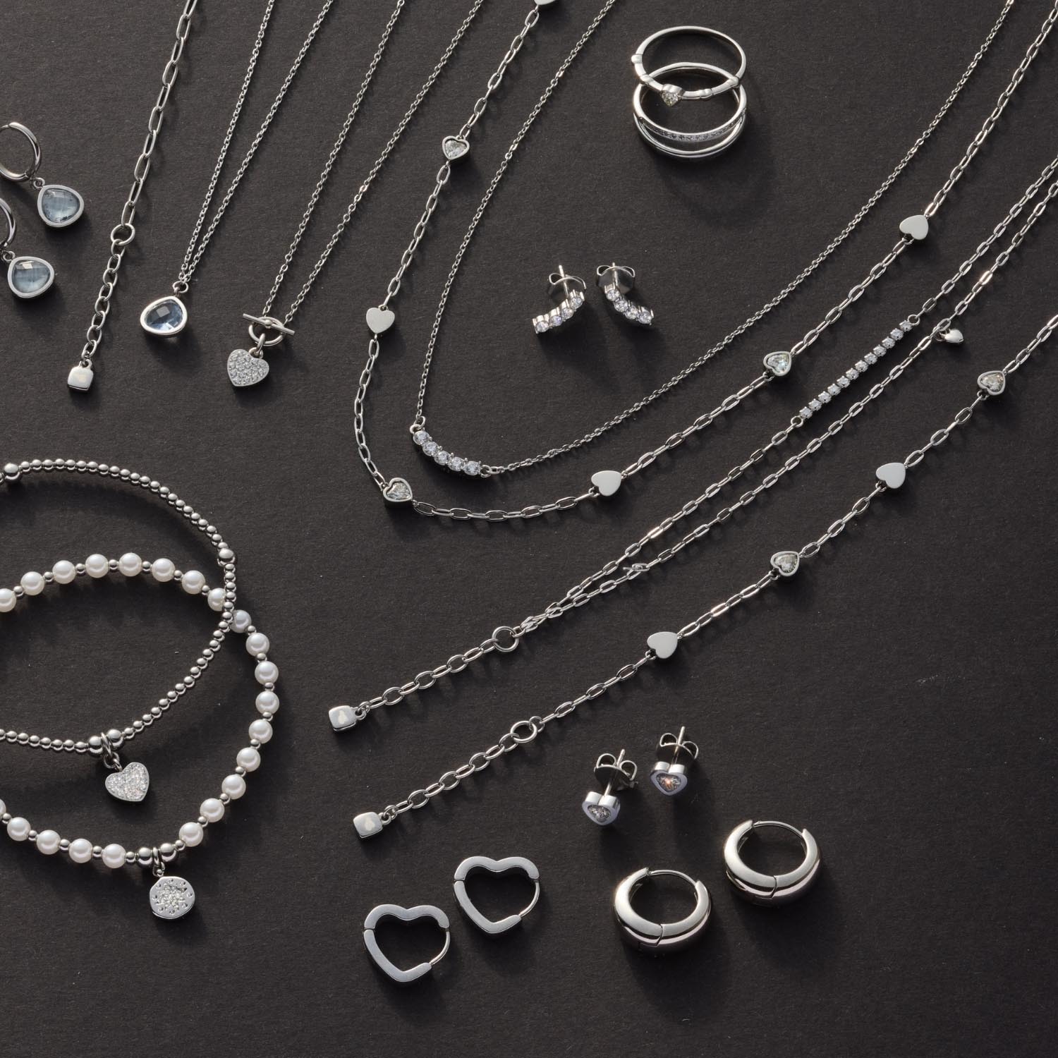 Silberner Schmuck auf dunklem Untergrund, Ohrstecker TINI CIAO zwischen Halsketten und Ringen