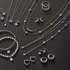 Silberner Schmuck auf dunklem Untergrund, Ohrstecker TINI CIAO zwischen Halsketten und Ringen