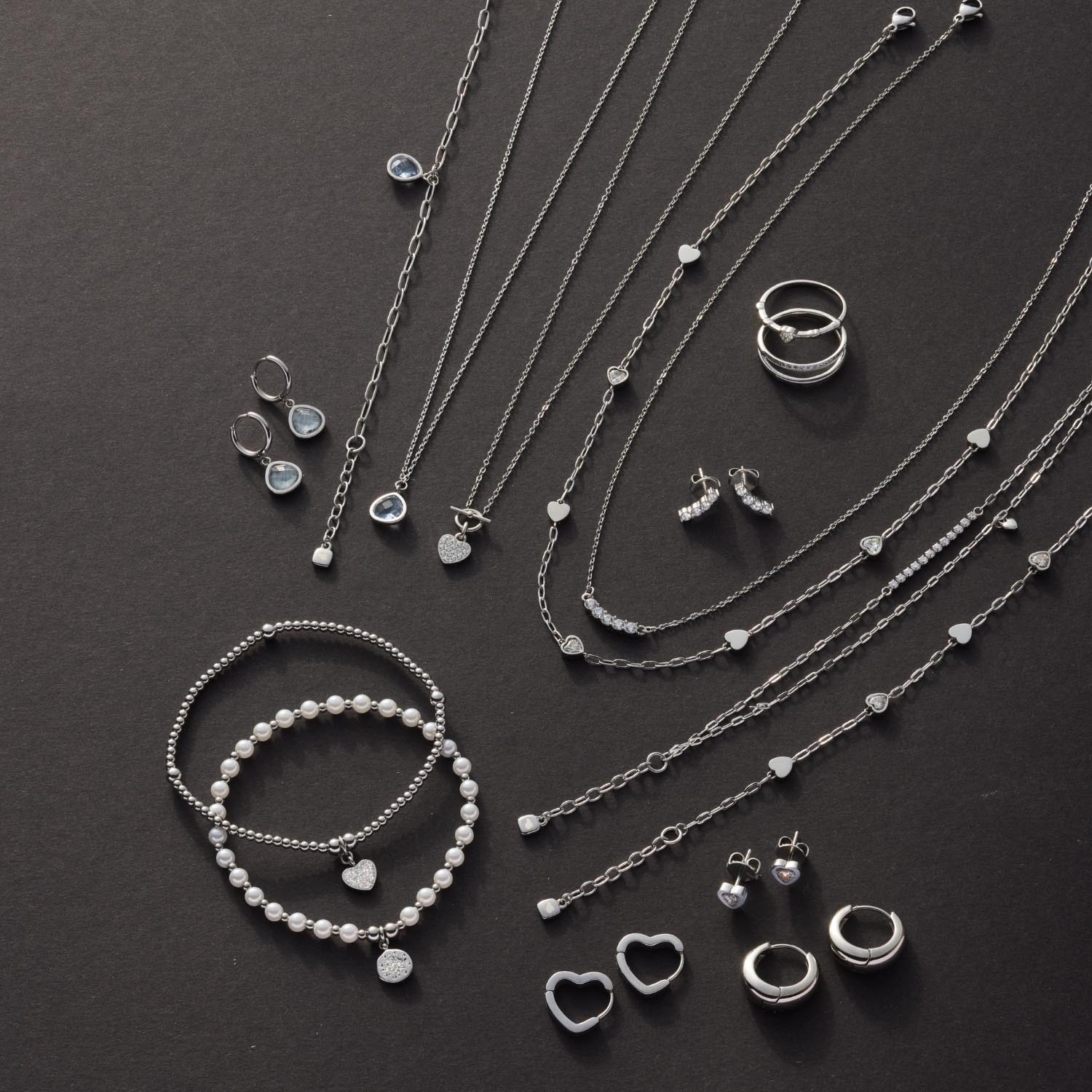Silberner Schmuck auf dunklem Hintergrund: Halsketten, Armbänder, Ringe und Ohrringe
