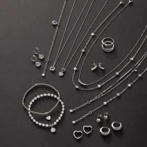 Silberner Schmuck auf dunklem Hintergrund: Halsketten, Armbänder, Ringe und Ohrringe