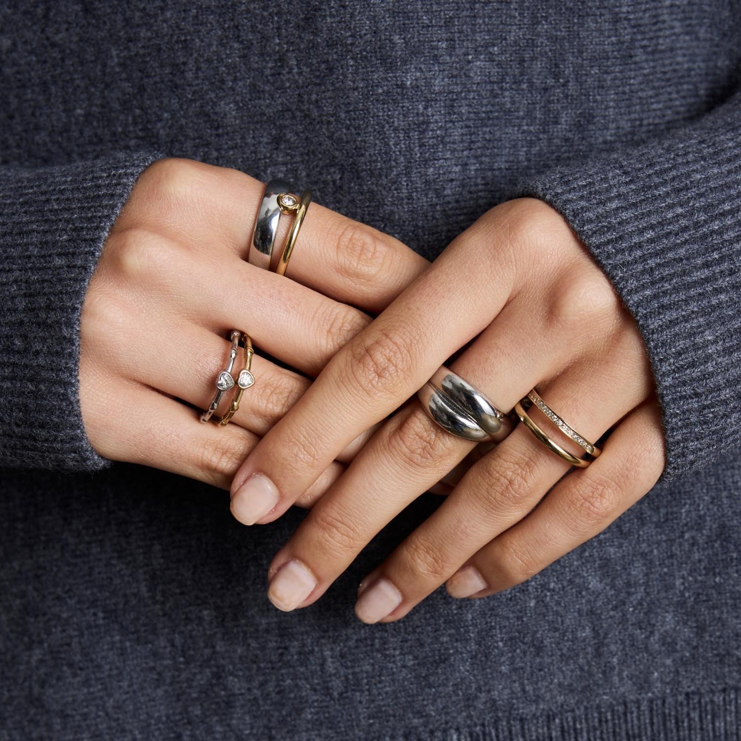 Hände mit mehreren goldenen Ringen, darunter Ring TINI 19 gold CIAO, an grauem Pullover