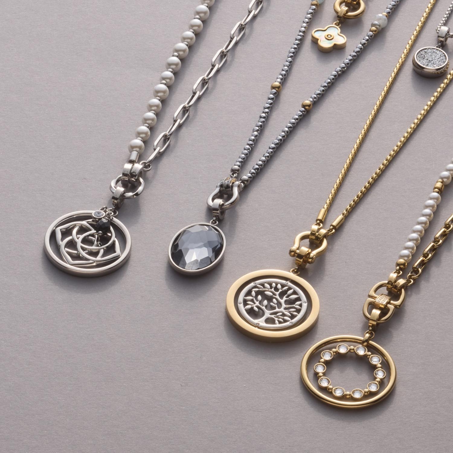 Mehrere Anhänger SYLVIA Clip & Mix in Gold und Silber an Ketten auf grauem Untergrund