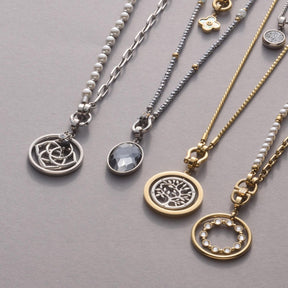 Mehrere Anhänger SYLVIA Clip & Mix in Gold und Silber an Ketten auf grauem Untergrund
