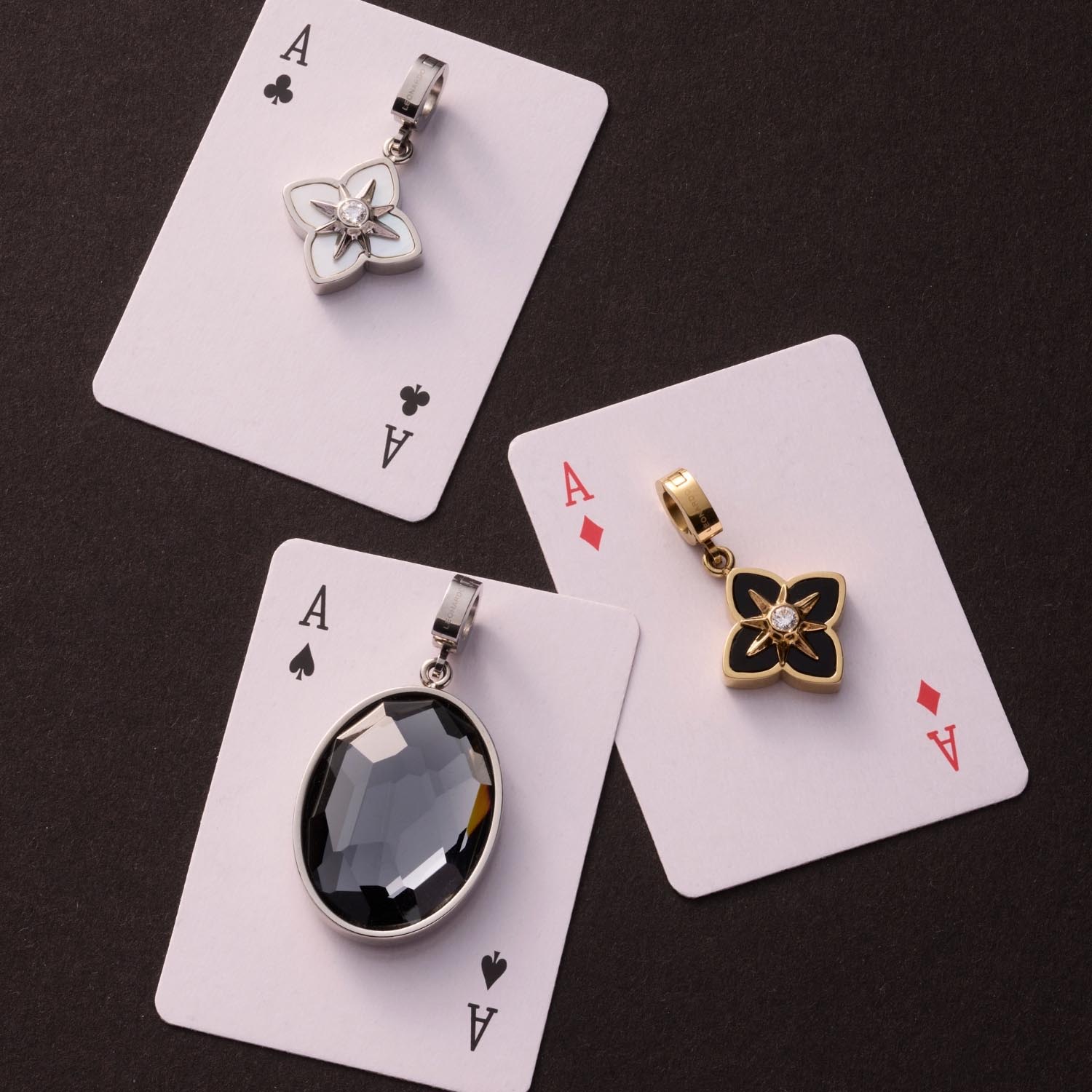 Drei Spielkarten mit silbernen und goldenen Anhängern auf dunklem Untergrund