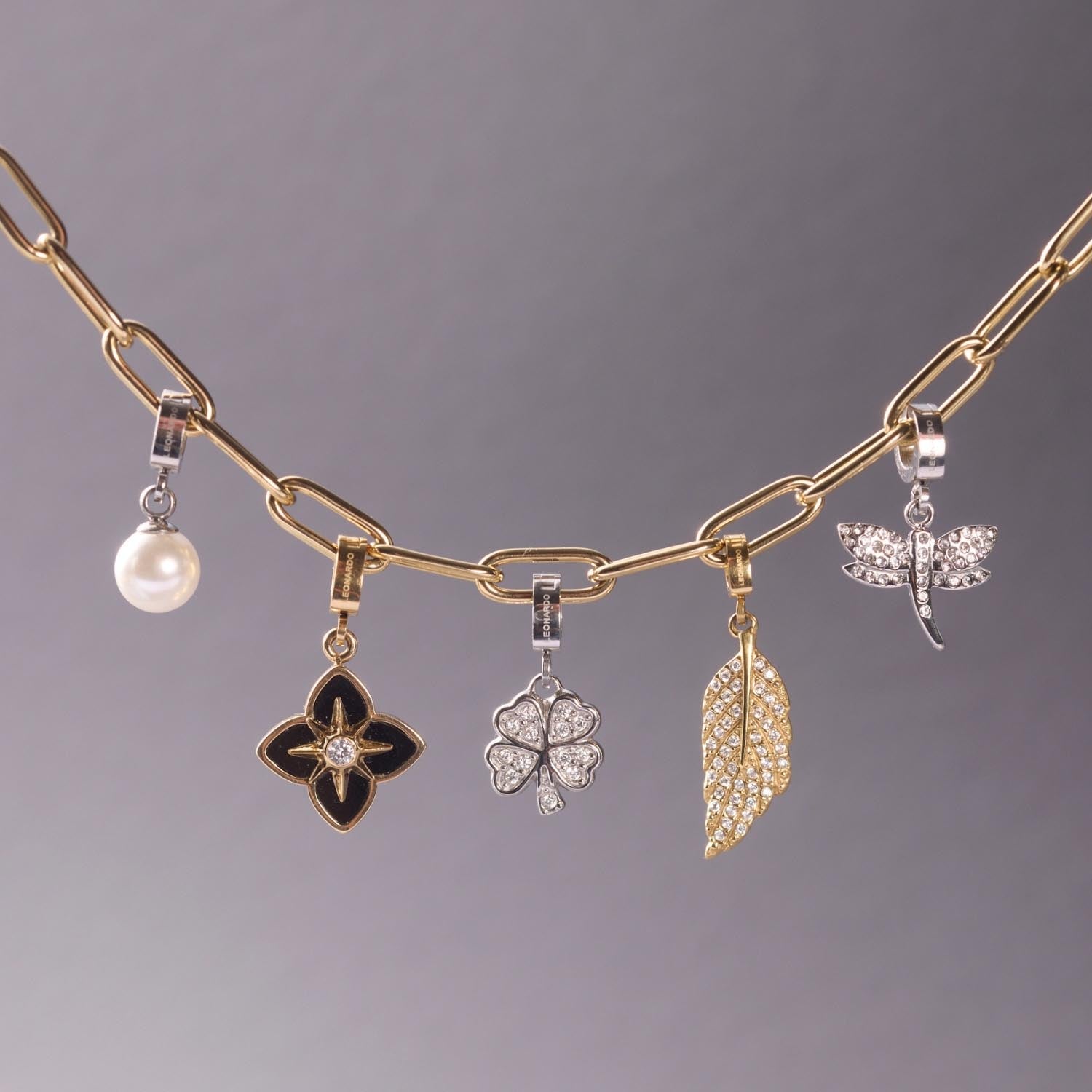 Anhänger FEDRA gold Clip & Mix mit fünf Charms an Kette gegen grauen Hintergrund