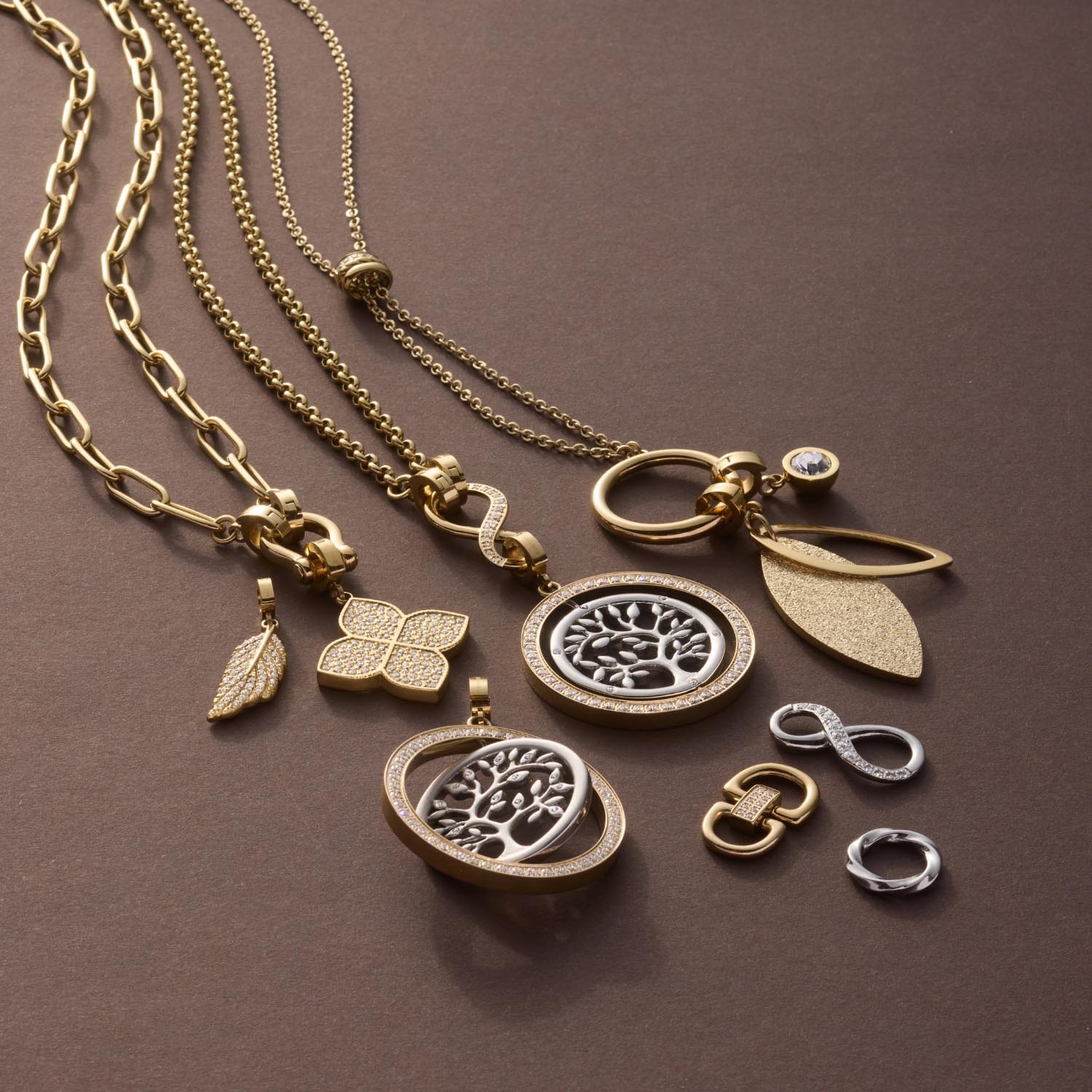 Goldene Schmuckanhänger und Ketten mit floralen Motiven und Schäkeln auf grauem Hintergrund