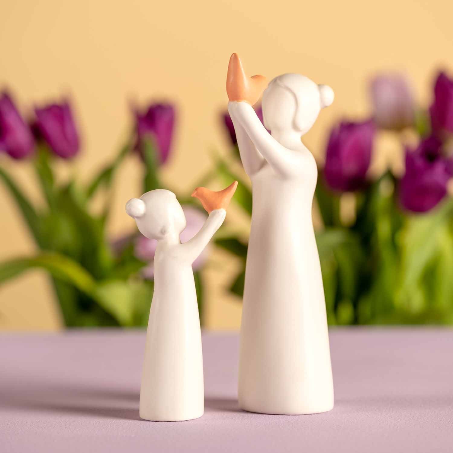 Weiße Keramikfigur Mädchen mit Vogel neben lila Tulpen