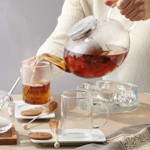Teekanne MOON wird über Tasse gegossen, gedeckter Tisch mit Gebäck