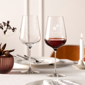 Rotweinglas BRUNELLI mit Gravur auf gedecktem Tisch, eines gefüllt mit Rotwein