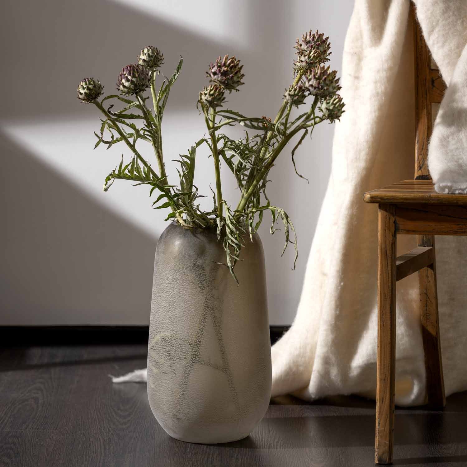 Vase TROGOLO mit getrockneten Blüten in hellem Wohnraum neben Textilien