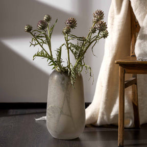 Vase TROGOLO mit getrockneten Blüten in hellem Wohnraum neben Textilien