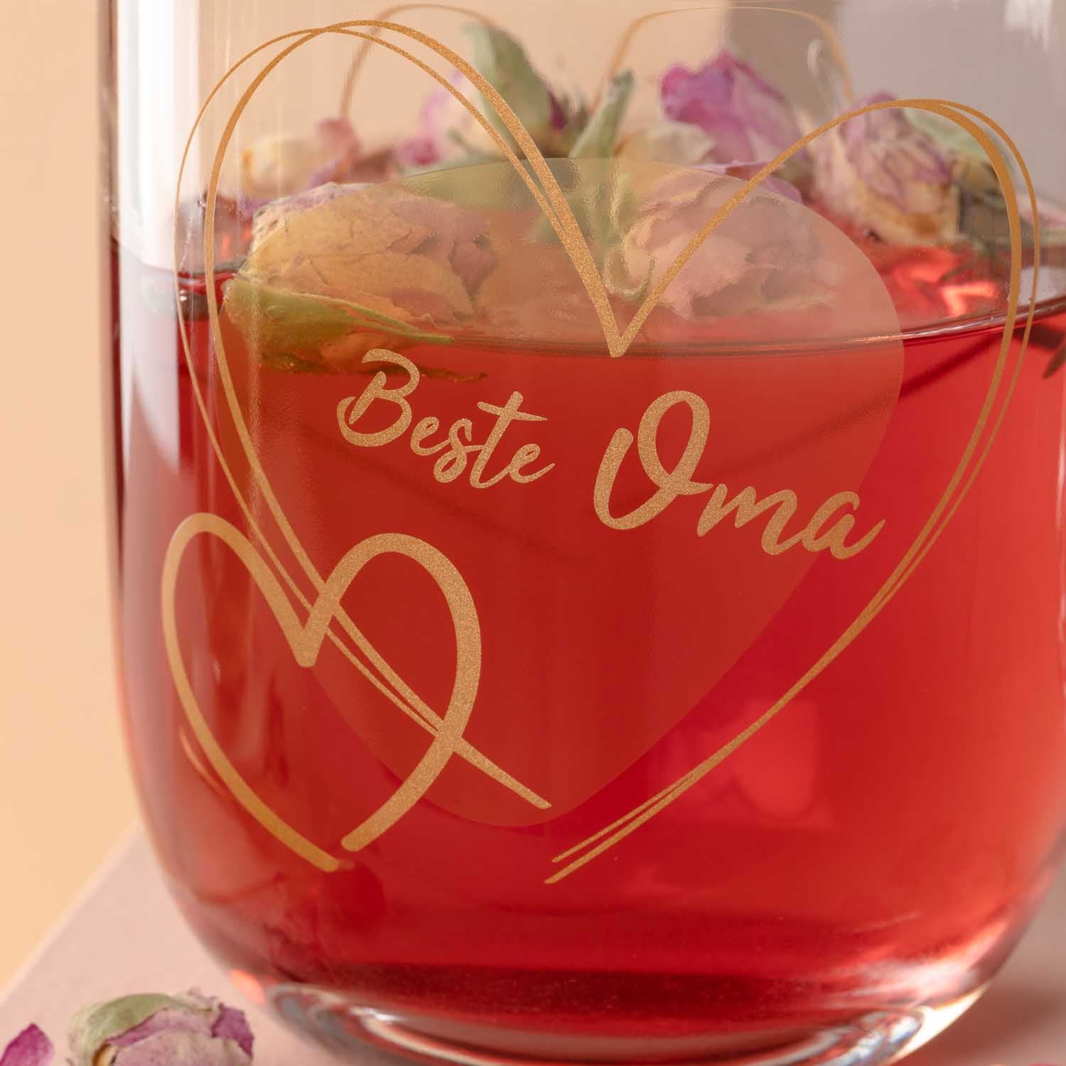 Glas mit roter Flüssigkeit, goldener Gravur "Beste Oma" und Herzdesign, gefüllt mit Blüten