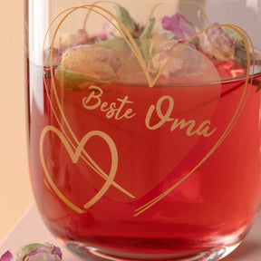 Glas mit roter Flüssigkeit, goldener Gravur "Beste Oma" und Herzdesign, gefüllt mit Blüten