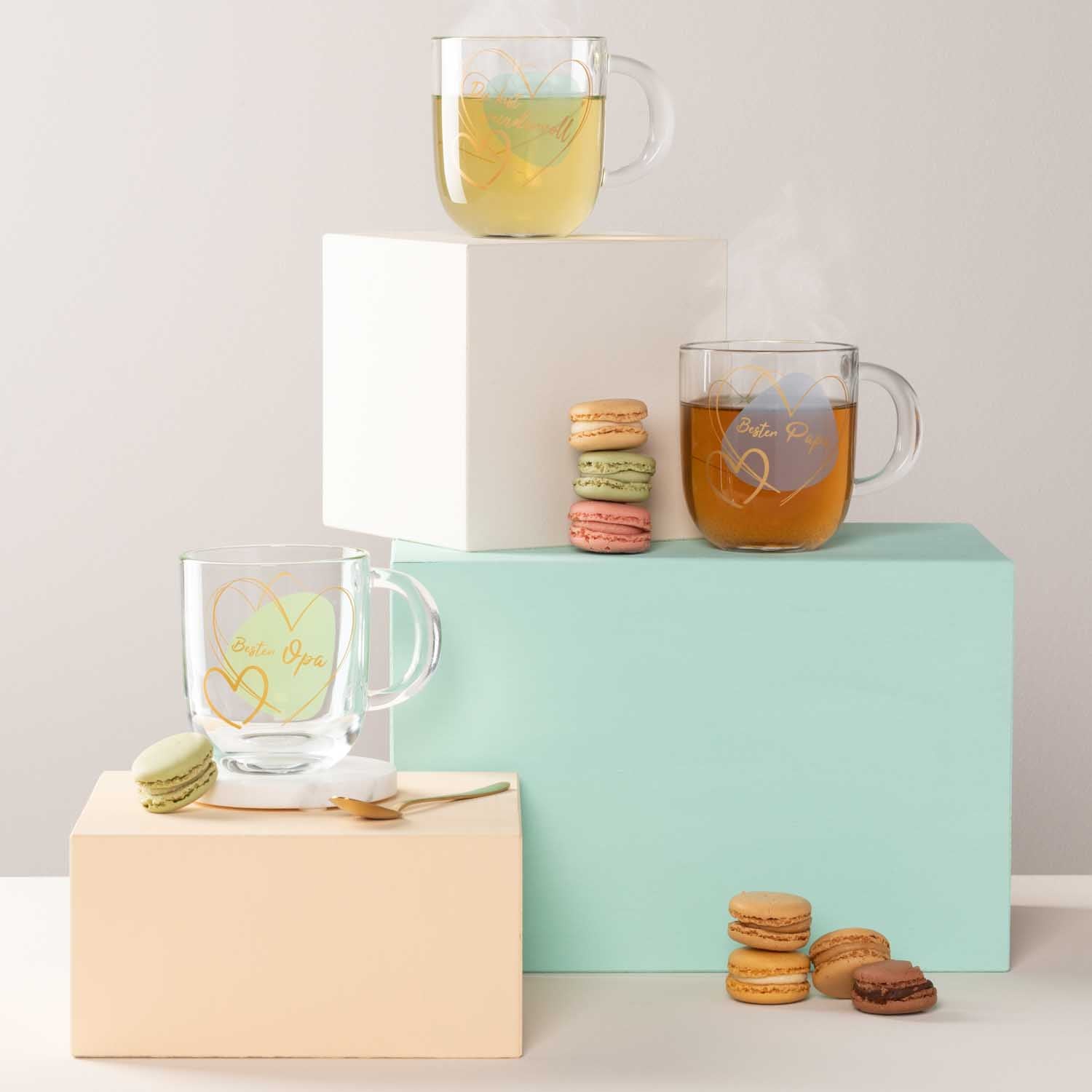 Glasbecher mit Tee auf Farbblöcken neben Macarons und weiteren Getränken