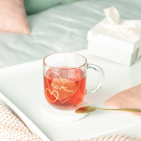 Glastasse EMOZIONE mit rotem Tee auf weißem Tablett, Gravur "Beste Mama" sichtbar
