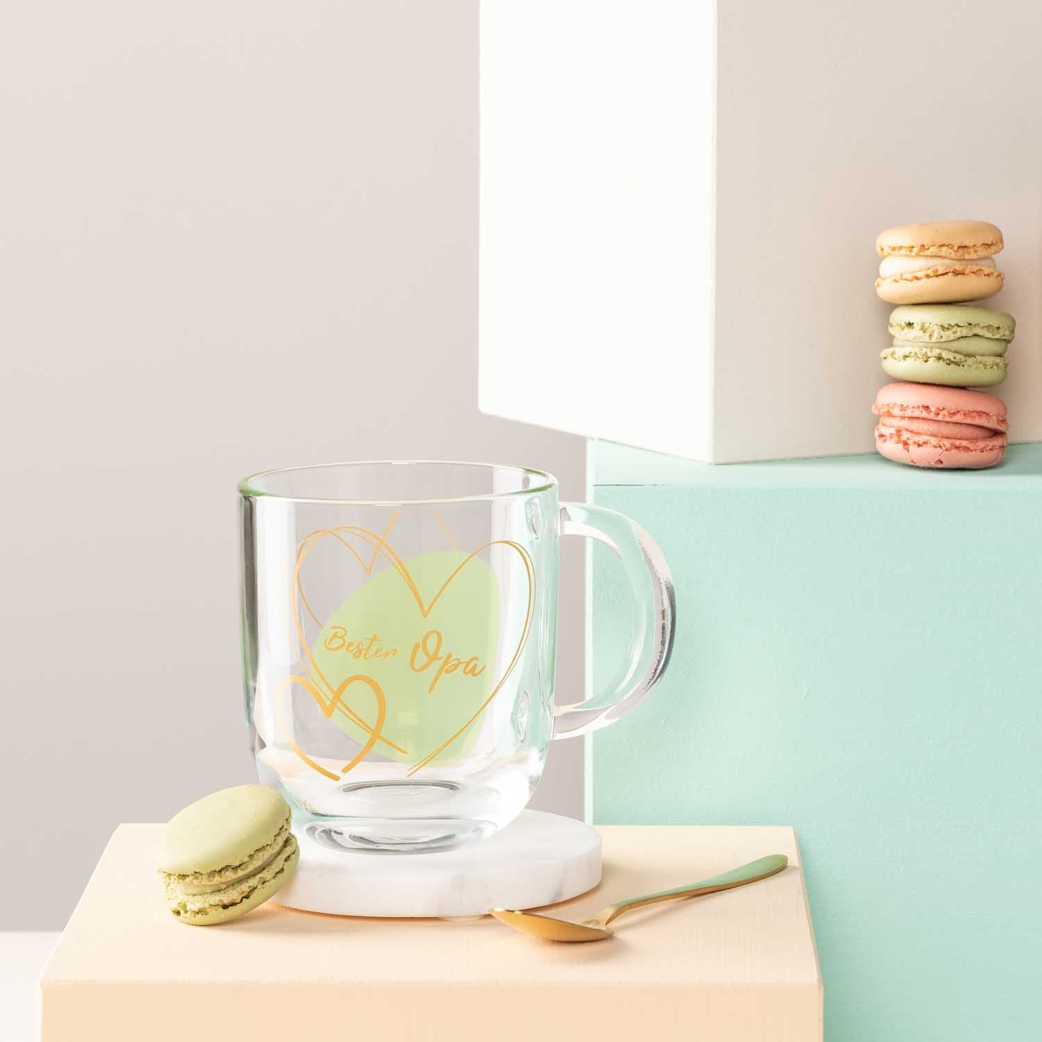 Glastasse mit gelber Gravur "Bester Papa", Macarons und Dekoobjekte auf farbigen Oberflaechen
