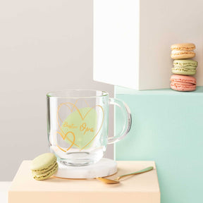 Glastasse mit gelber Gravur "Bester Papa", Macarons und Dekoobjekte auf farbigen Oberflaechen