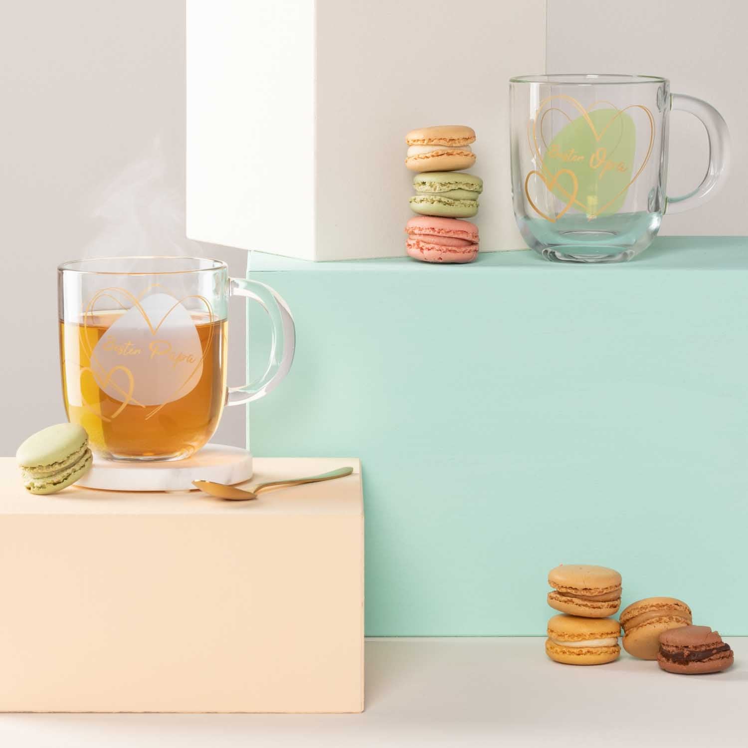Glastasse mit Getränk und Eiswürfeln, Macarons und Dekoblöcken auf farbigem Hintergrund