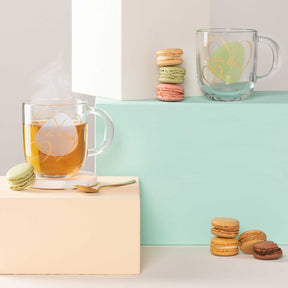 Glastasse mit Getränk und Eiswürfeln, Macarons und Dekoblöcken auf farbigem Hintergrund