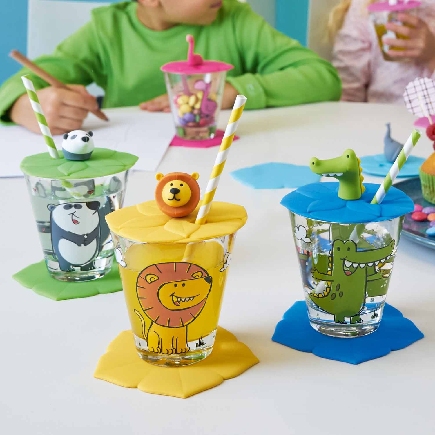 Kindertrinksets mit Tiermotiven und farbigen Deckeln auf Kindertisch, Kind im grünen Shirt
