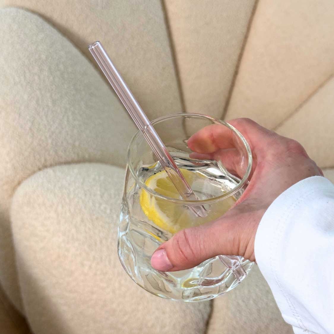 Person hält Glas mit Glastrinkhalm und Zitronenscheibe in der Hand