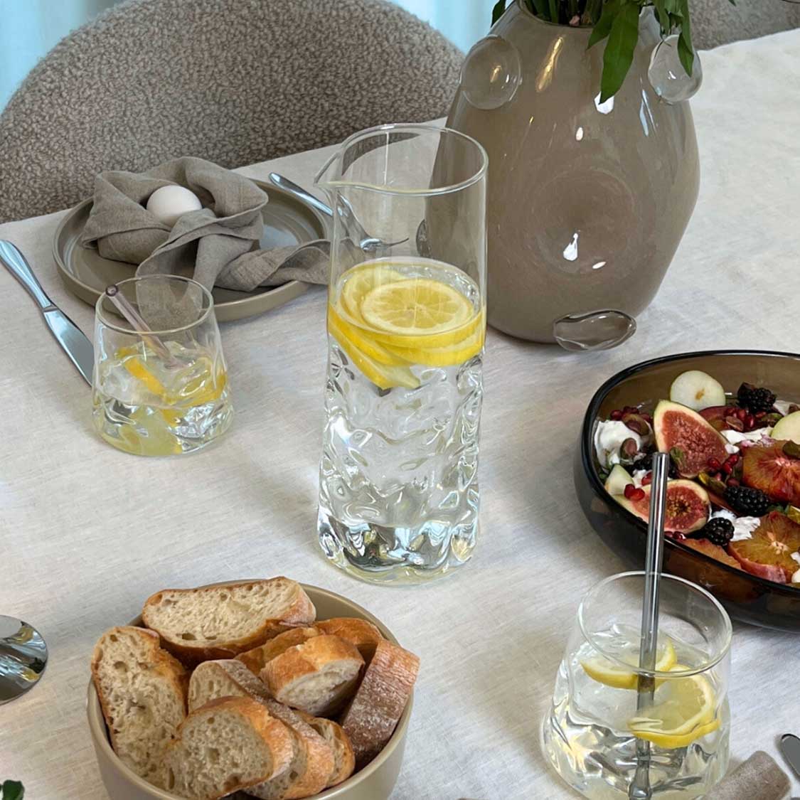 Gedeckter Tisch mit Glastrinkhalmen in Wassergläsern, Brot und Feigen