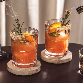 Zwei gefüllte Trinkgläser SPIRITII NOVA mit orangefarbenem Cocktail, Eiswürfeln, Rosmarin und Zitronenscheibe auf Untersetzer