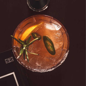 Trinkglas SPIRITII NOVA mit orangebraunem Cocktail, Eiswürfeln und Jalapeño-Scheiben als Garnitur