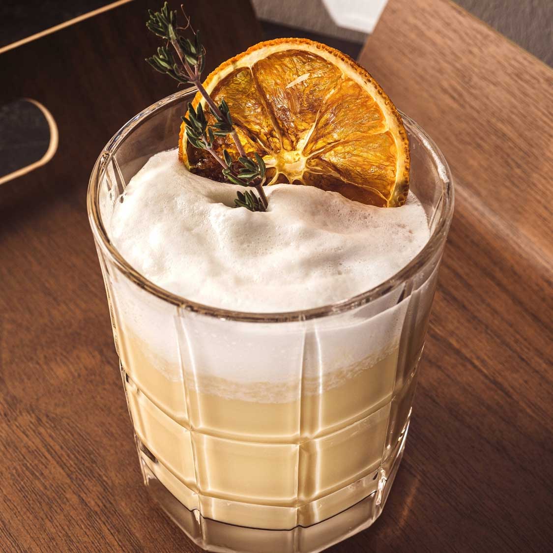 Trinkglas SPIRITII NOVA mit Cocktail, Orangenscheibe und Kräutern auf Holztisch