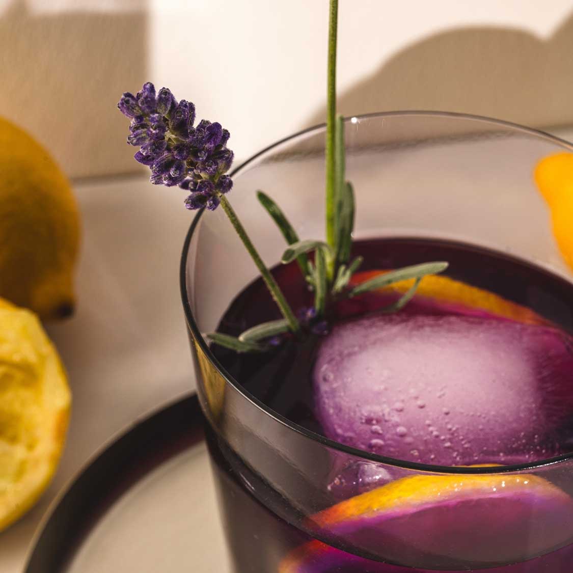 Trinkglas LEGGERO mit lila Getränk, Zitronenscheiben und Lavendelblüte als Tischdeko