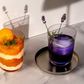 Trinkglas LEGGERO mit lila Getränk, Lavendelblüten, neben Cocktail mit Orangenscheibe