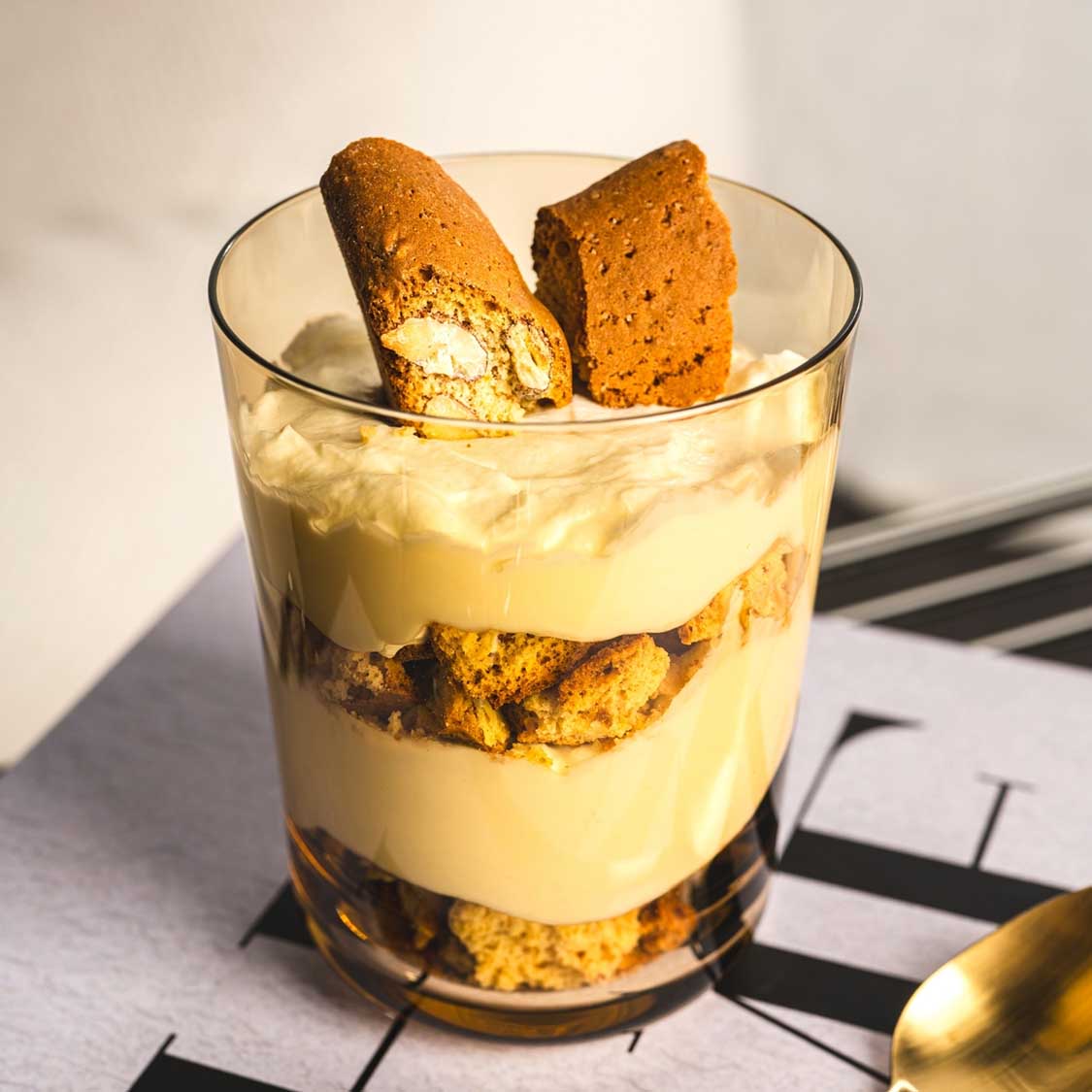 Trinkglas LEGGERO mit Creme-Dessert und Keksen gefüllt auf gemustertem Untergrund
