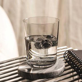 Trinkglas LEGGERO mit Wasser und Eiswürfeln auf grauem Untersetzer, Notizbuch im Hintergrund