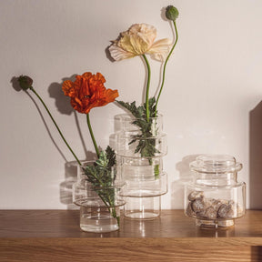 Klare Glasdosen mit Blumen in Vasen auf Holztisch arrangiert