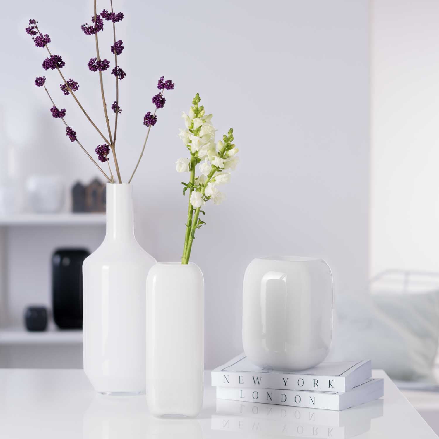 Drei weiße Glasvasen mit Blumen in Wohnzimmer-Szenerie