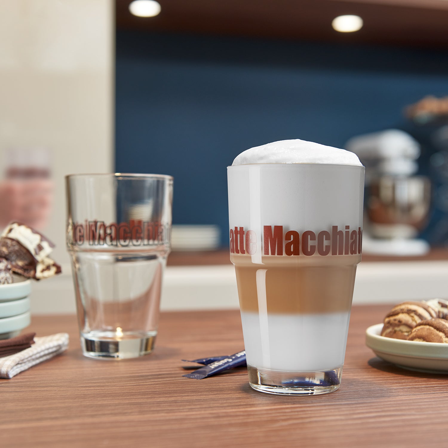Becher SOLO mit Latte Macchiato auf gedecktem Tisch, Glas und Gebäck