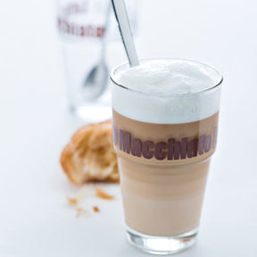 Becher SOLO mit Latte Macchiato, daneben Gebäck und Wasserglas