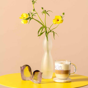 Vase VIVACE mit gelben Blüten, Tasse und Früchten auf gelbem Tisch